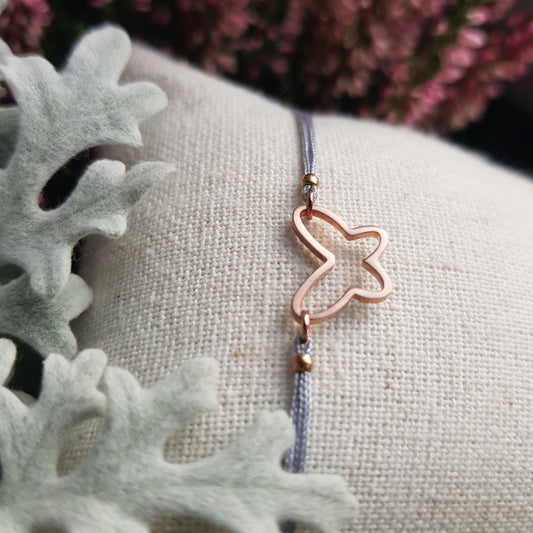 Zartes Makramee-Armband aus grauem Band mit roségold Schmetterlings-Anhänger auf Schmuckkissen