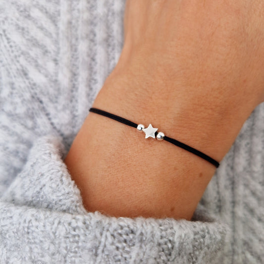 Makramee-Armband aus schwarzem Band mit zwei Silber-Perlen und Silber-Stern-Perle am Handgelenk des Models in Nahaufnahme