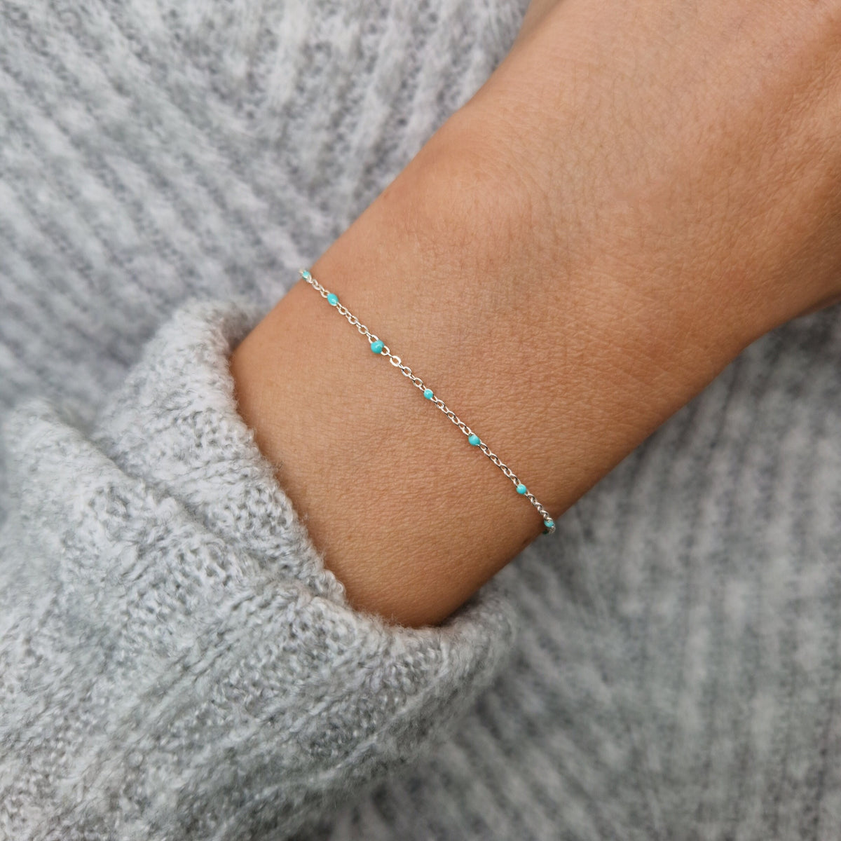 Zartes 925-Silber-Armband aus einer Ankerkette mit türkisen Perlen aus Emaille am Handgelenk des Models in Nahaufnahme von oben