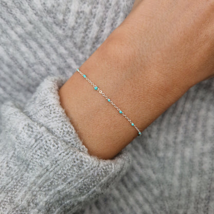 Zartes 925-Silber-Armband aus einer Ankerkette mit türkisen Perlen aus Emaille am Handgelenk des Models in Nahaufnahme von oben