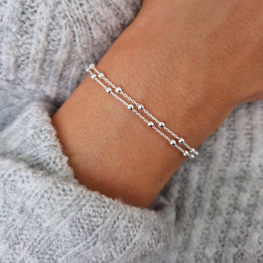 Doppeltes, filigranes 925-Silber-Satelliten-Armband am Handgelenk des Models in Nahaufnahme von oben