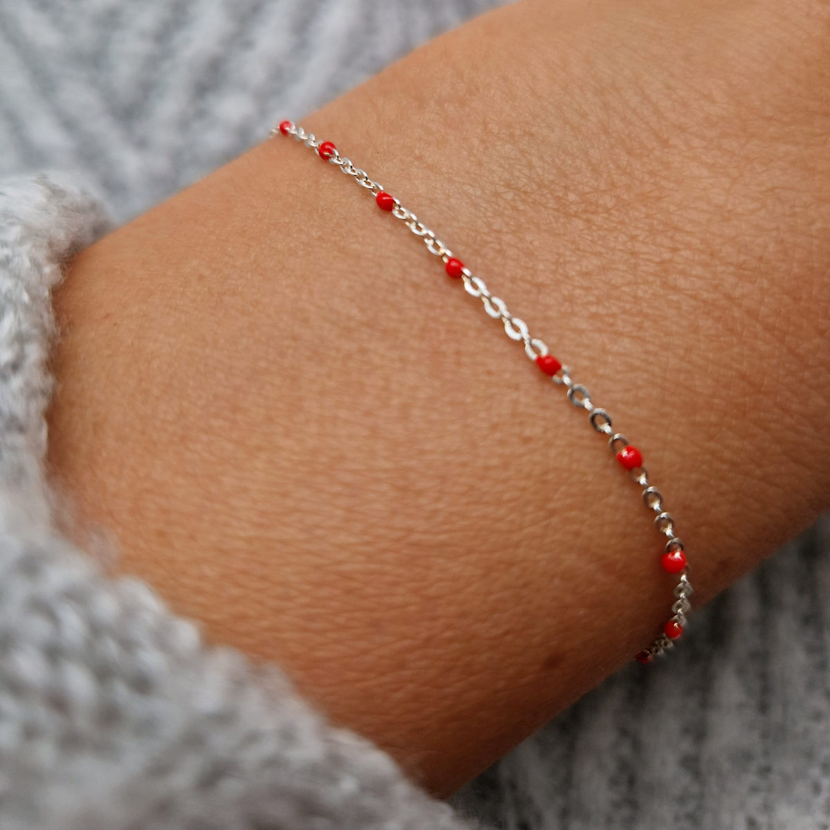 Zartes 925 Silber-Armband aus einer Ankerkette mit roten Perlen aus Emaille am Handgelenk des Models.