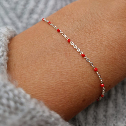 Zartes 925 Silber-Armband aus einer Ankerkette mit roten Perlen aus Emaille am Handgelenk des Models.