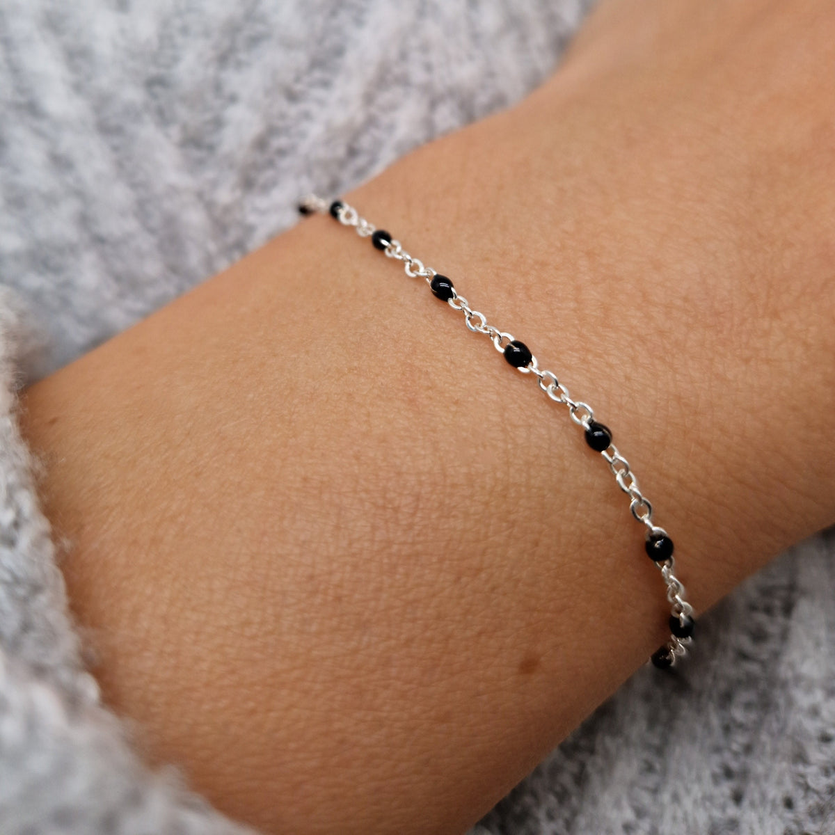 Zartes Armband aus einer Ankerkette mit schwarzen Perlen aus Emaille am Handgelenk des Models in seitlicher Nahaufnahme