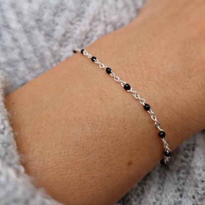 Zartes Armband aus einer Ankerkette mit schwarzen Perlen aus Emaille am Handgelenk des Models in seitlicher Nahaufnahme