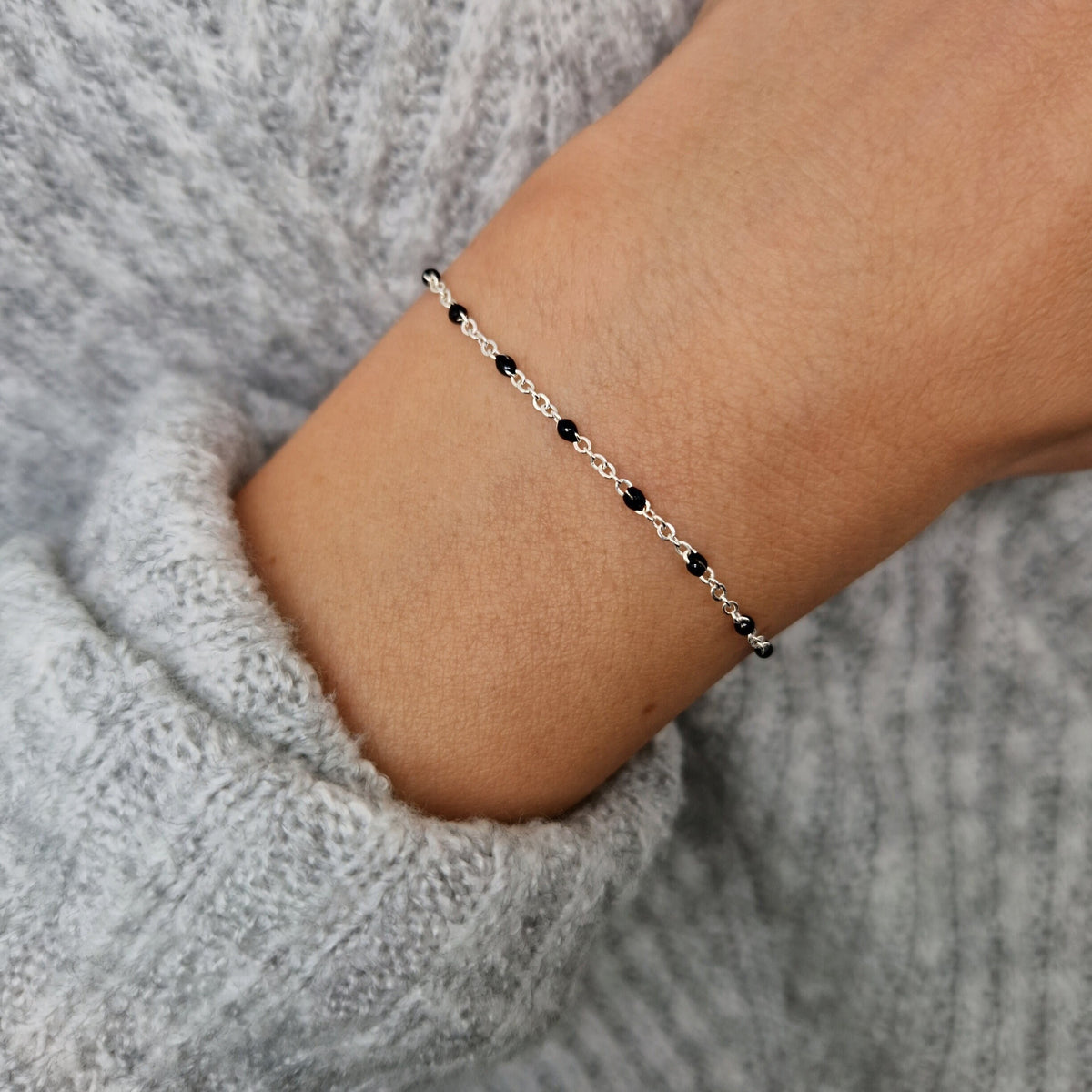 Zartes 925 Silber-Armband aus einer Ankerkette mit schwarzen Perlen aus Emaille am Handgelenk des Models in Nahaufnahme
