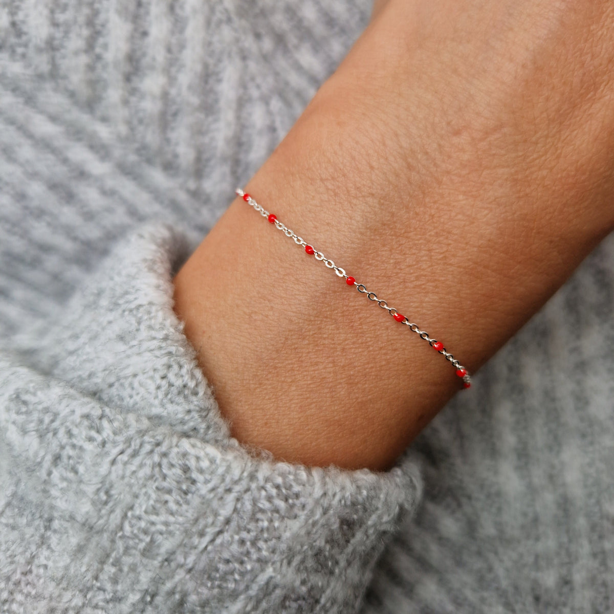 Zartes 925 Silber-Armband aus einer Ankerkette mit roten Perlen aus Emaille am Handgelenk des Models.