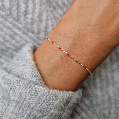 Zartes 925 Silber-Armband aus einer Ankerkette mit roten Perlen aus Emaille am Handgelenk des Models.