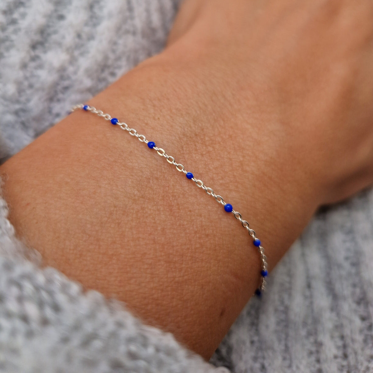 Zartes Armband aus einer Ankerkette mit blauen Perlen aus Emaille am Handgelenk des Models