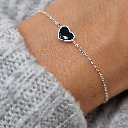 Zartes Silberarmband mit glänzendem schwarzem Herz aus Silber am Handgelenk des Models