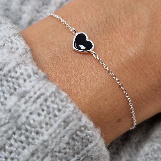 Zartes Silberarmband mit glänzendem schwarzem Herz aus Silber am Handgelenk des Models
