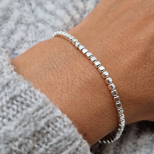 Breites massives Silberarmband mit rechteckigen Perlen am Handgelenk des Models in Nahaufnahme mit hellgrauem Pulli