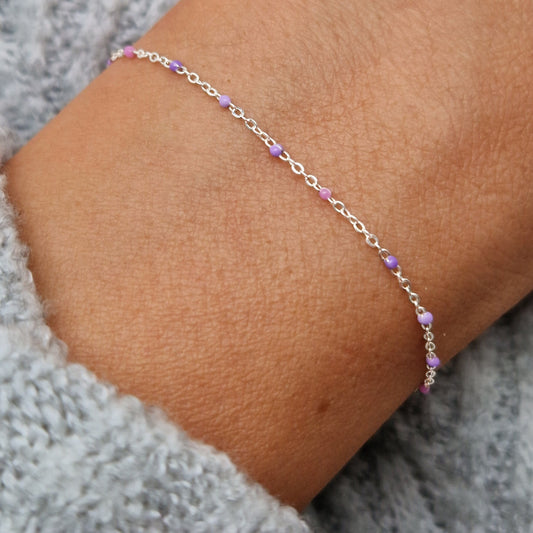 Zartes 925 Silber-Armband aus einer Ankerkette mit lila und fliederfarbenen Perlen aus Emaille am Handgelenk des Models in Nahaufnahme