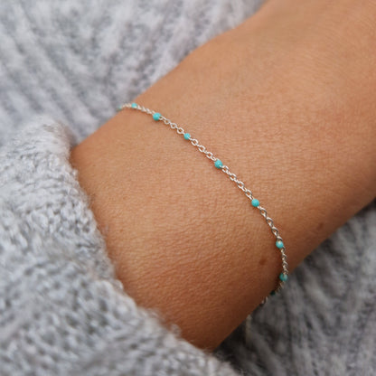 Zartes Armband aus einer Ankerkette mit türkisen Perlen aus Emaille am Handgelenk des Models in seitlicher Nahaufnahme