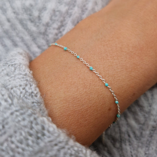 Zartes Armband aus einer Ankerkette mit türkisen Perlen aus Emaille am Handgelenk des Models in seitlicher Nahaufnahme