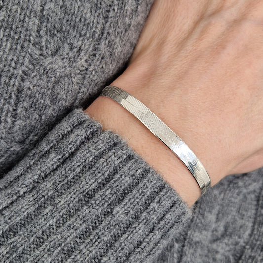 Massives sehr breites Schlangenarmban am Handgelenk des Models in seitlicher Nahaufnahme mit dunkelgrauem Pulli