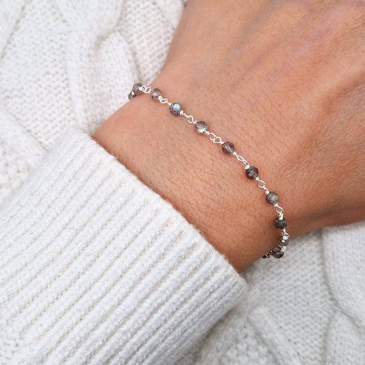 zartes Silber Armband mit grauen transparenten facettierten Labradorit Perlen aus Naturstein am Handgelenk des Models in seitlicher Nahaufnahme mit weißem Pulli