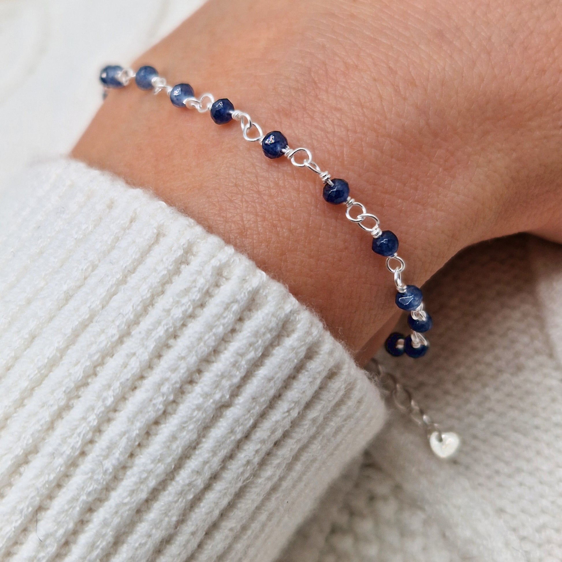 zartes Silber Armband mit dunkelblauen Jade Perlen aus Naturstein am Handgelenk des Models in seitlicher Nahaufnahme mit weißem Pulli aus Wolle