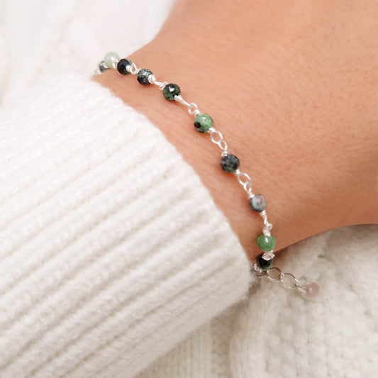 zartes Silber Armband mit grau grünen facettierten Zoisit  Perlen aus Naturstein am Handgelenk des Models in seitlicher Nahaufnahme mit weißem Pulli aus Wolle