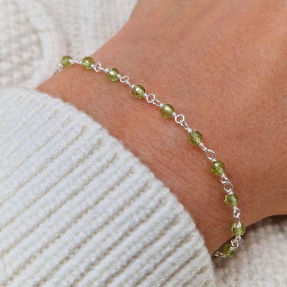 zartes Silber Armband mit grünen transparenten facettierten Peridot Perlen aus Naturstein am Handgelenk des Models in seitlicher Nahaufnahme mit weißem Pulli