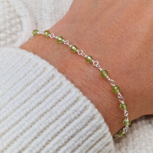zartes Silber Armband mit grünen transparenten facettierten Peridot Perlen aus Naturstein am Handgelenk des Models in seitlicher Nahaufnahme mit weißem Pulli
