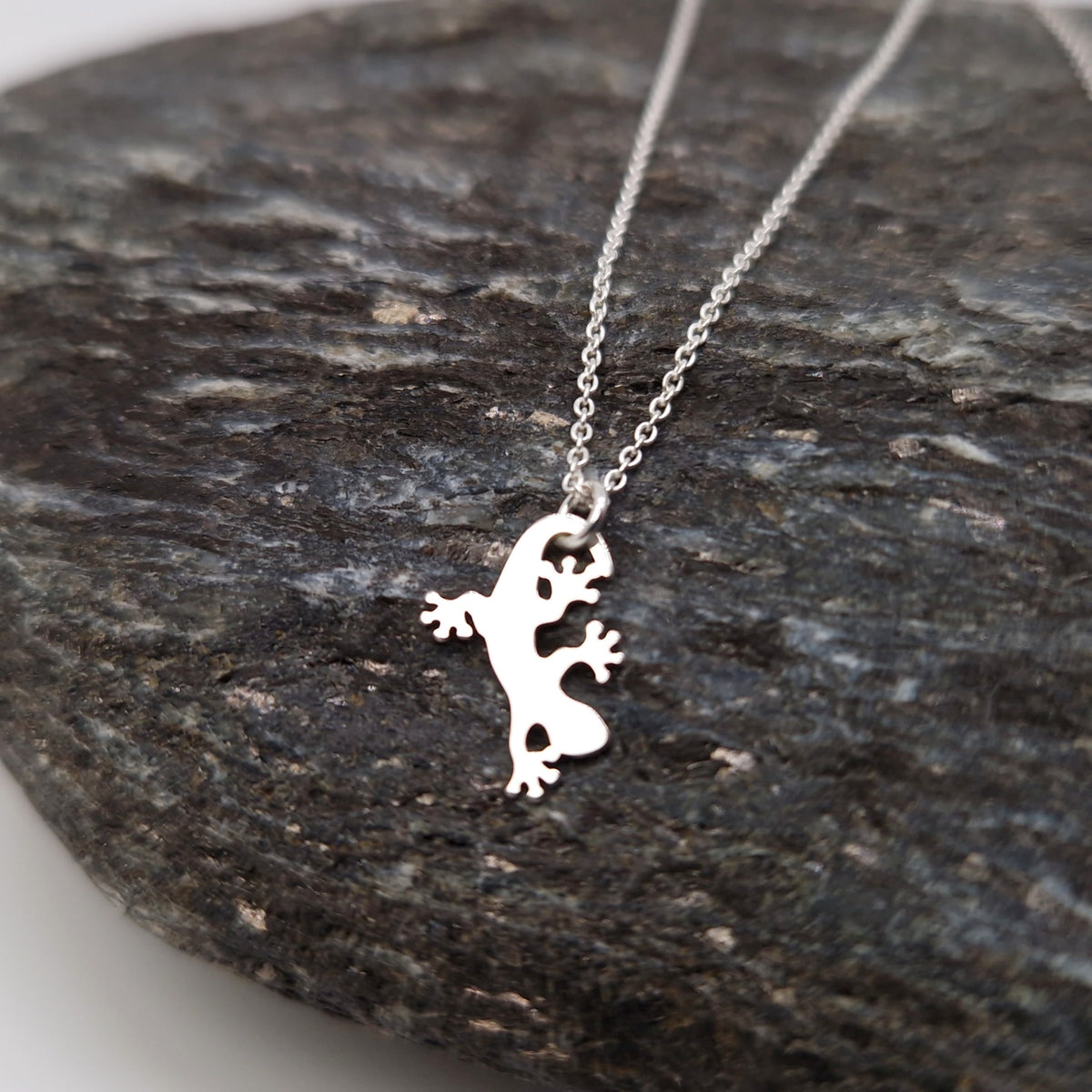 Ankerkette aus 925 Sterling Silber mit flachem Eidechsen-Anhänger aus Silber auf dunklem Stein fotografiert