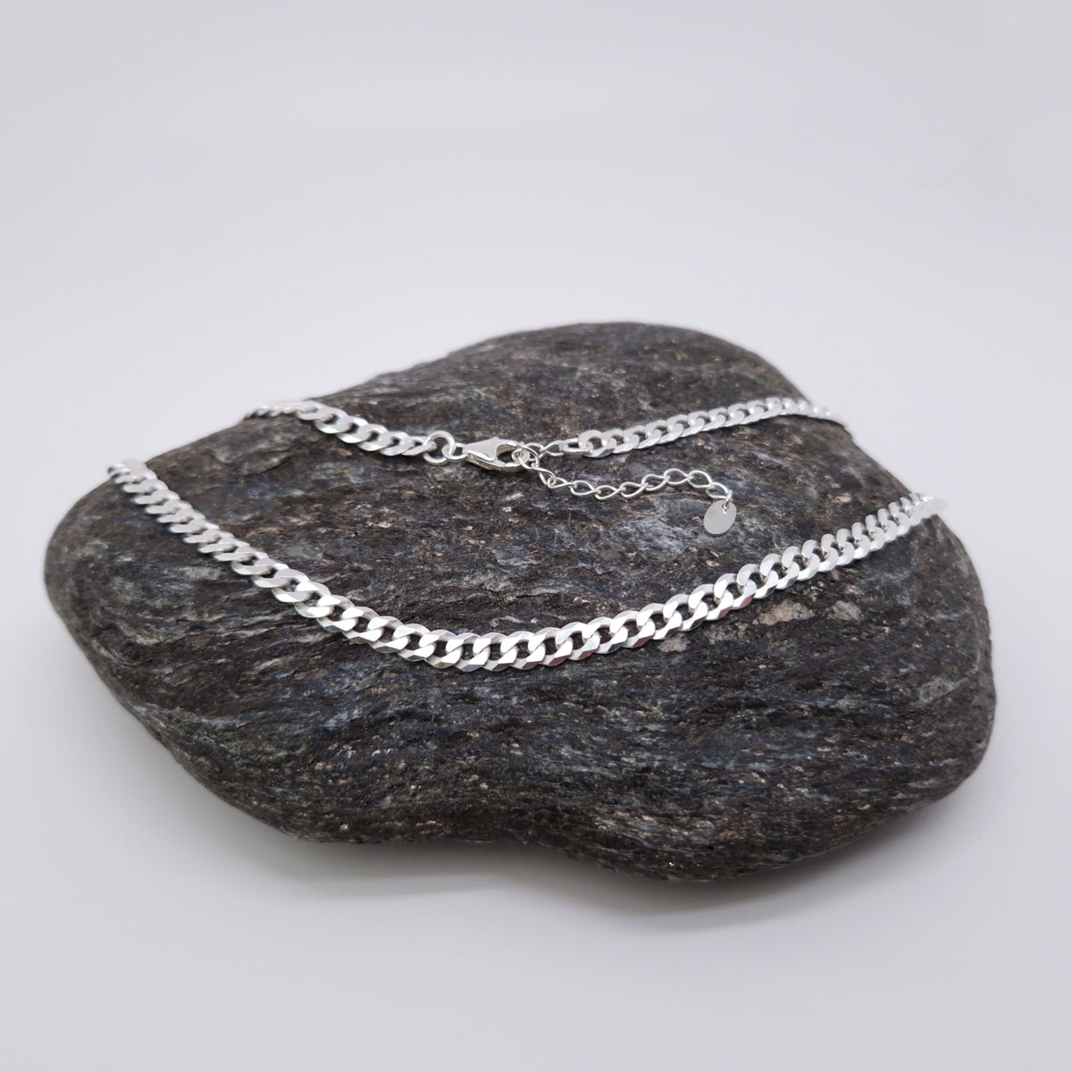 Breite flache Panzerkette mit großen Kettengliedern aus massivem 925 Sterling Silber mit Verlängerungskettchen und kleinem Herzanhänger am Verlängerungskettchen auf einem dunklen Stein fotografiert