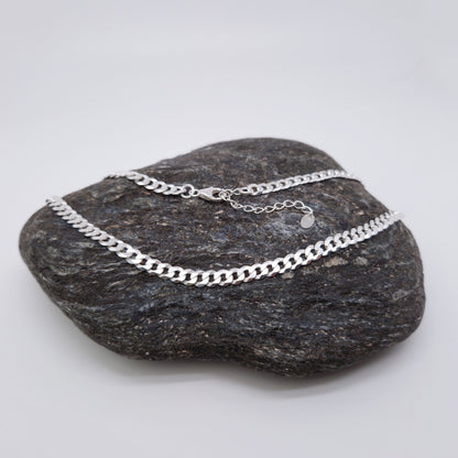 Breite flache Panzerkette mit großen Kettengliedern aus massivem 925 Sterling Silber mit Verlängerungskettchen und kleinem Herzanhänger am Verlängerungskettchen auf einem dunklen Stein fotografiert