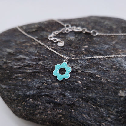 Halskette aus massivem 925 Sterling Silber mit emaillierter, fünfblättriger, runder Blüte in türkis mit Loch in der Mitte mit Verlängerungskettchen und kleinem Herz am Verlängerungskettchen auf einem dunklem Stein