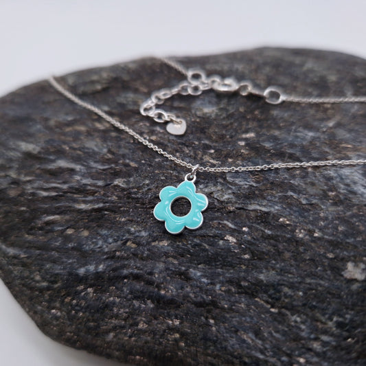 Halskette aus massivem 925 Sterling Silber mit emaillierter, fünfblättriger, runder Blüte in türkis mit Loch in der Mitte mit Verlängerungskettchen und kleinem Herz am Verlängerungskettchen auf einem dunklem Stein