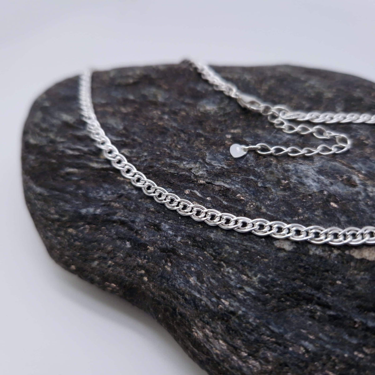 Breite  gewebte Halskette aus massivem 925 Sterling Silber. Die einzelnen Kettenglieder sind doppelreihig. Durch die kleine Verlängerungskette mit angehängtem kleinen Herzchen ist die Kette größenverstellbar.  Foto zeigt die Kette auf dunklem Stein.