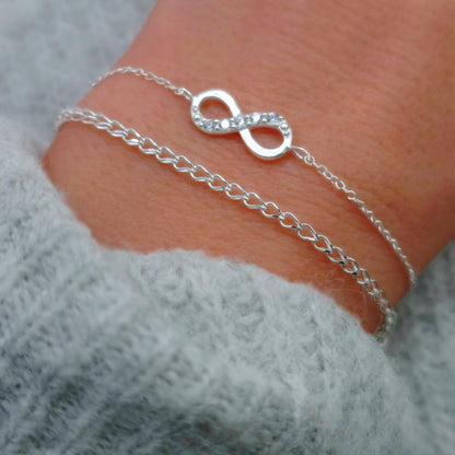 zartes  gewebtes Silber Armband am Handgelenk des Models in seitlicher Nahaufnahme mit hellgrauem Pulli kombiniert mit zartem SilbernArmband mit Unendlichkeitssymbol und Zirkoniakristallen